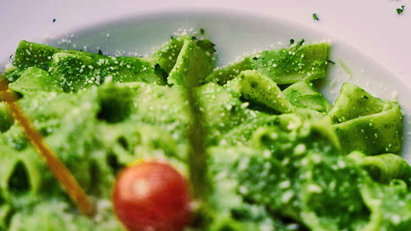 plato blanco con pasta verde con un tomate cherry