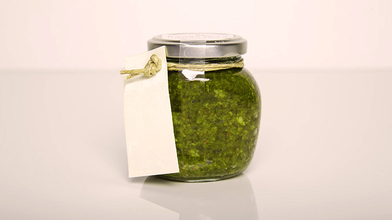 bote de cristal cerrado sobre un fondo un poco anaranjado que está relleno de salsa verde y que tiene una cuerda con un papel atado