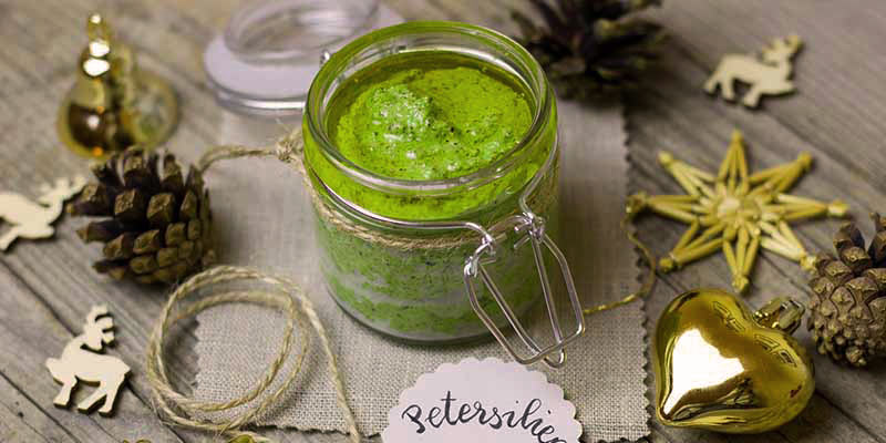 mesa de madera gris con un bote de cristal con salsa verde que está rodeado de decoraciones de navidad, como una estrella dorada, una piña, renos y un corazón dorado