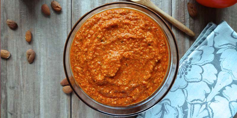 bol de cristal con salsa que está rodeado de un mantel de flores y almendras