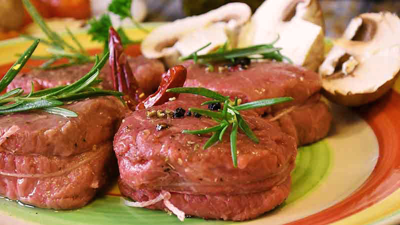 carne de ternera cruda con hierba y champiñones crudos sobre un plato rojo, amarillo, blanco y verde