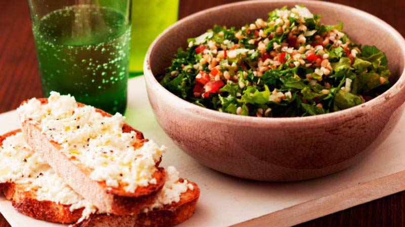 bol marron con ensalada y unos panes en la izquierda, así como también un vaso de cristal