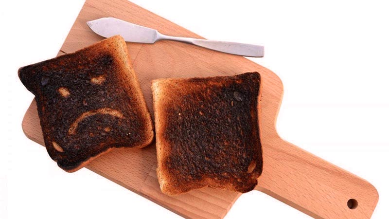 tabla de madera sobre un fondo blanco y con dos tostadas quemadas con un cuchillo al lado. Una de las tostadas tiene dibujada una cara triste