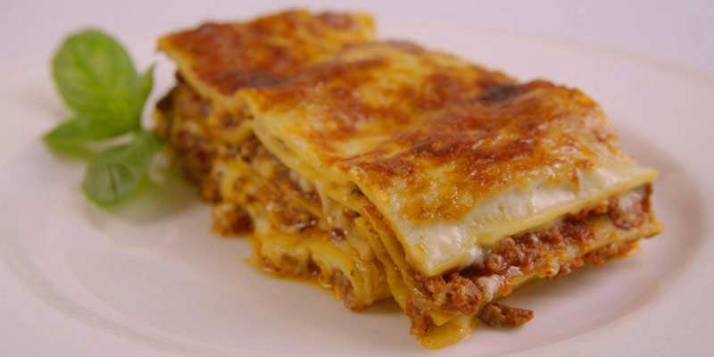 trozo de fragmento de lasaña de atún con unas hojas verdes a un lado en un plato blanco