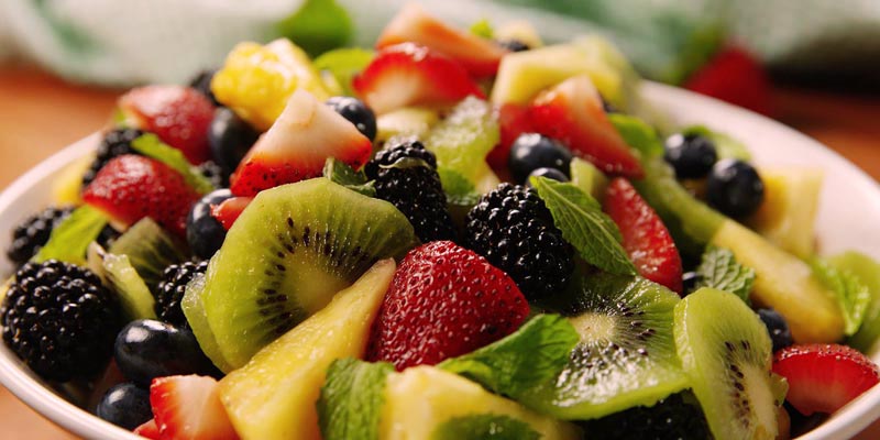 plato blanco con fruta cortada como kiwi, fresas, moras, hojas, arándanos y piña