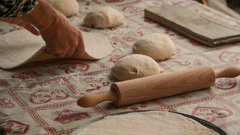 dos manos sosteniendo una masa aplanada sobre una mesa con bolas de masa y un rodillo