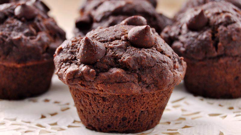 cuatro muffins hechos de chocolate con pepitas encima. Tan solo el que está más cerca está enfocado