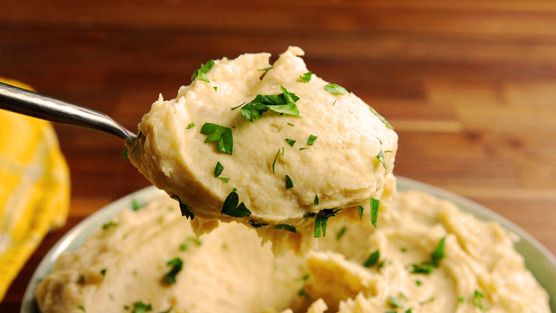 una cuchara metálica sosteniendo parte del puré que hay debajo en un plato