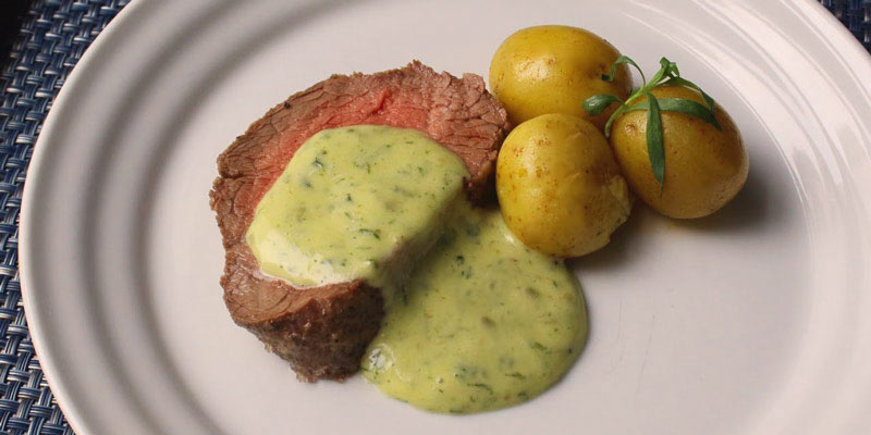 filete de carne con salsa y tres patatas pequeñas con piel, todo junto en un plato blanco