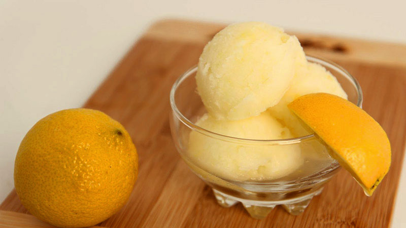 bol de cristal con helado de limón, un limón entero a un lado y una rodaja en el borde del bol
