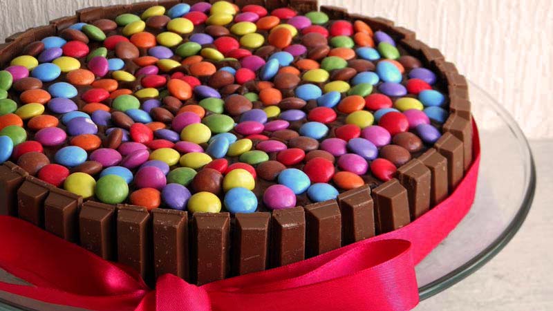 tarta con kit kats y lacasitos, además de un lazo rosa y sobre un plato de cristal