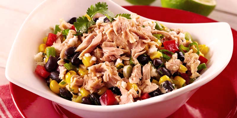 plato blanco con ensalada de atún, el cual está sobre otro plato rojo