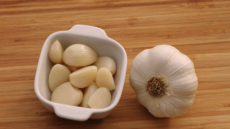 recipiente blanco con dientes de ajo pelados y con un manojo de ajos entero