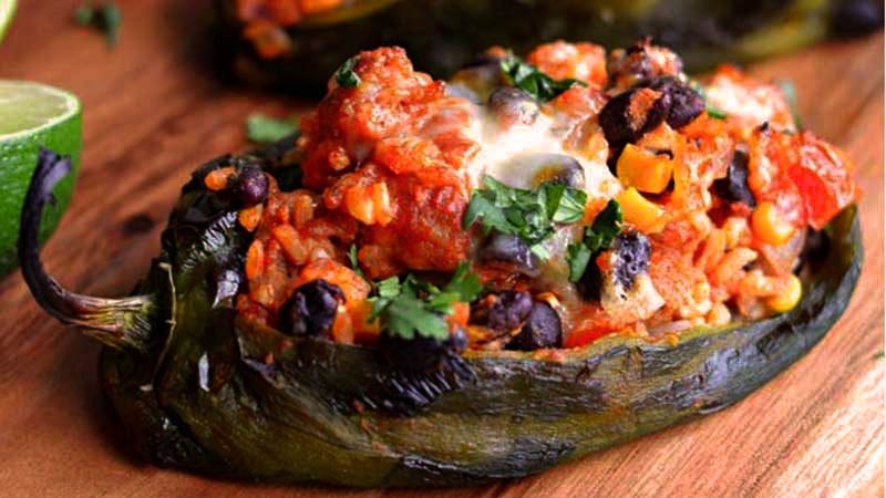un chile relleno sobre una mesa de madera y con una lima al lado