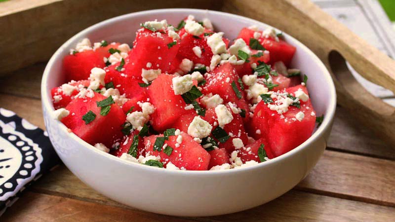 bol blanco con sandía y queso sobre una bandeja de madera