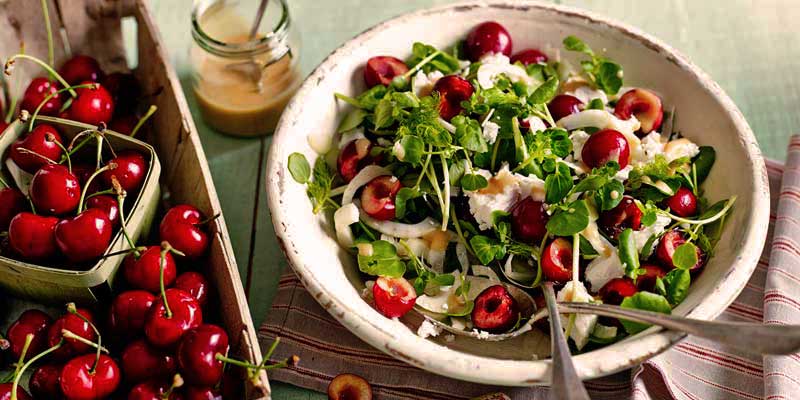 plato blanco con ensalada de cerezas y con una bandeja con cerezas al lado