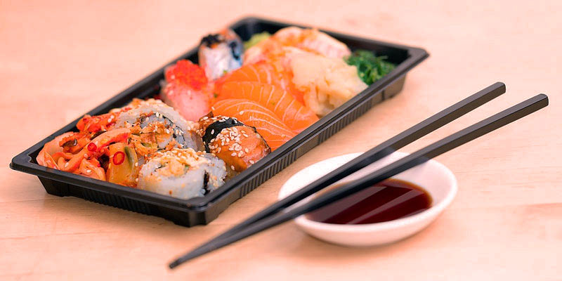 sushi puesto en una bandeja negra con unos palillos negros al lado y sobre un fondo de color melocotón