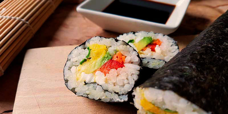 piezas de sushi sobre una tabla de madera y con un bol al fondo con salsa de soja