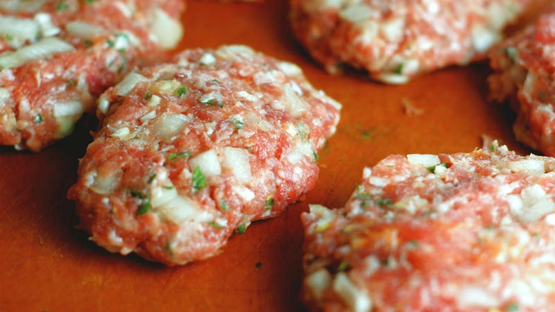 bolas de hamburguesa sin cocinar sobre una superficie naranja