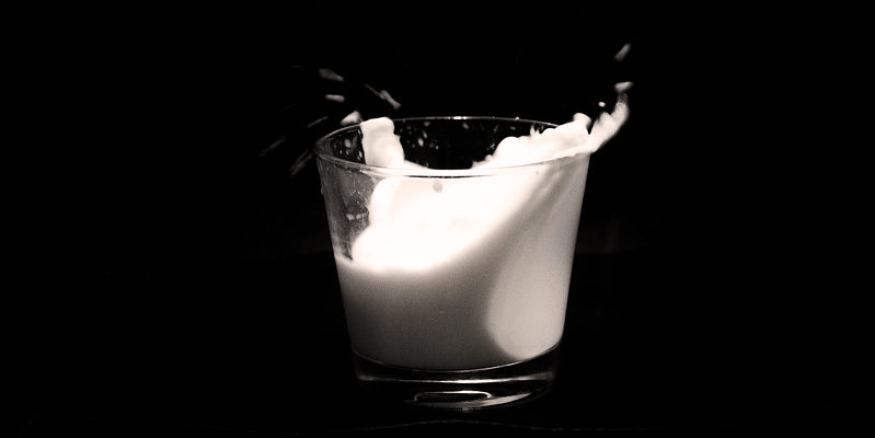 vaso de cristal con leche saliendo fuera con un fondo negro