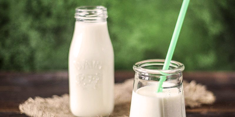 vaso de cristal con leche con una pajita verde y un tarro de leche detrás