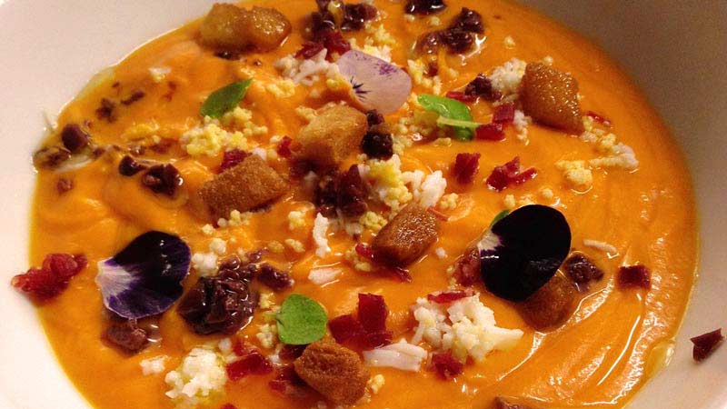 salmorejo con flores, queso, y jamón en un plato blanco