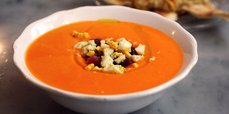 salmorejo en un plato blanco y con ingredientes como queso y jamón en el centro