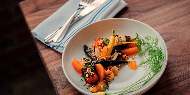 plato hondo blanco con verduras saldeadas y que está sobre una mesa de madera