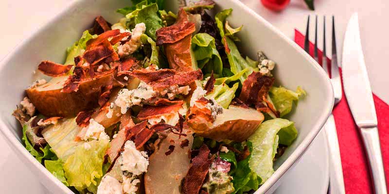 ensalada en un plato blanco cuadrado con cubiertos al lado sobre una servilleta rosa