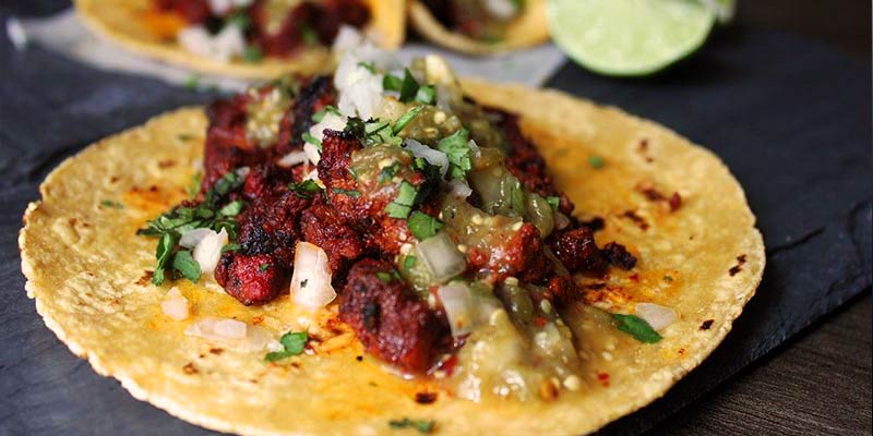 taco con carne y cebolla sobre un mantel azul y con más tacos al fondo