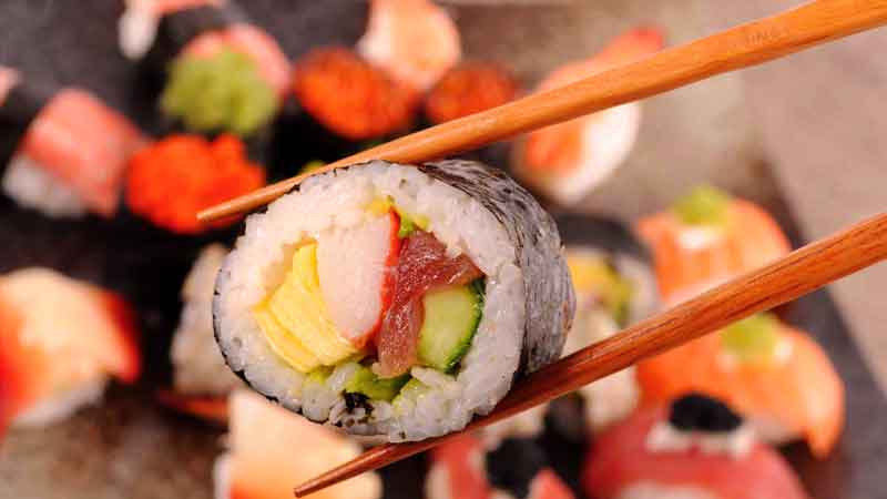unos palillos chinos sosteniendo una pieza de sushi con mucho más en el fondo desenfocados