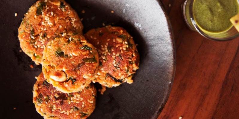 croquetas indias en un plato negro con salsa verde en un tarro al lado