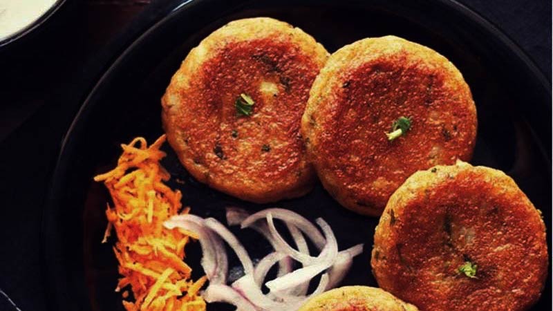 croquetas indias en un plato negro con cebolla y zanahoria troceada
