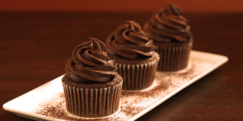 tres cupcakes en un recipiente blanco y rectangular en un fondo marrón