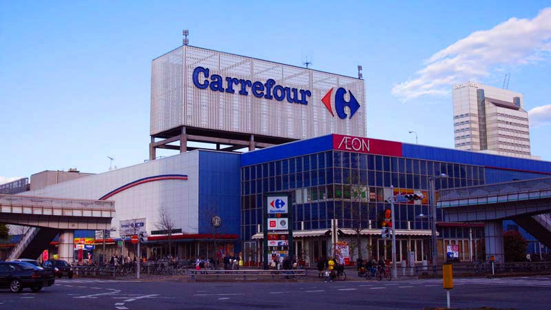 supermercado carrefour con cielo azul y un coche a la izquierda