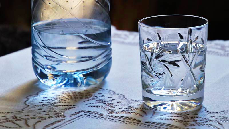 vaso de agua de cristal con una botella al lado