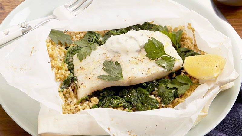 pescado en quinoa, limón y perejil sobre un plato blanco