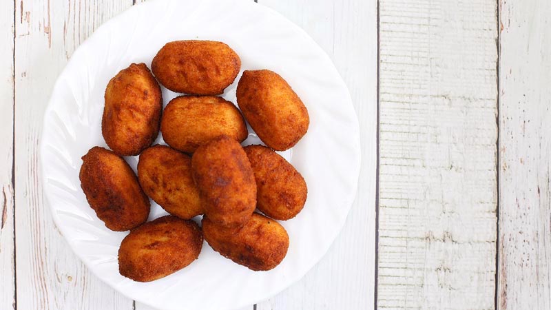 10 croquetas sobre un plato blanco y con un fondo de madera blanca