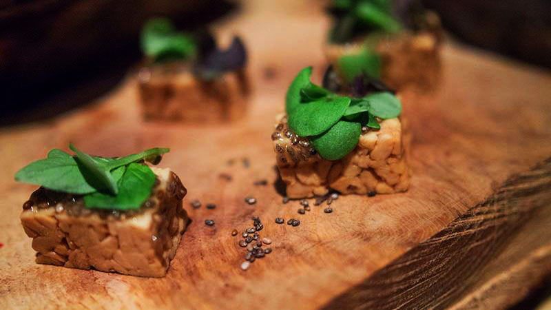 tempeh cortado en cuadrados con unas hoja encima y sobre madera