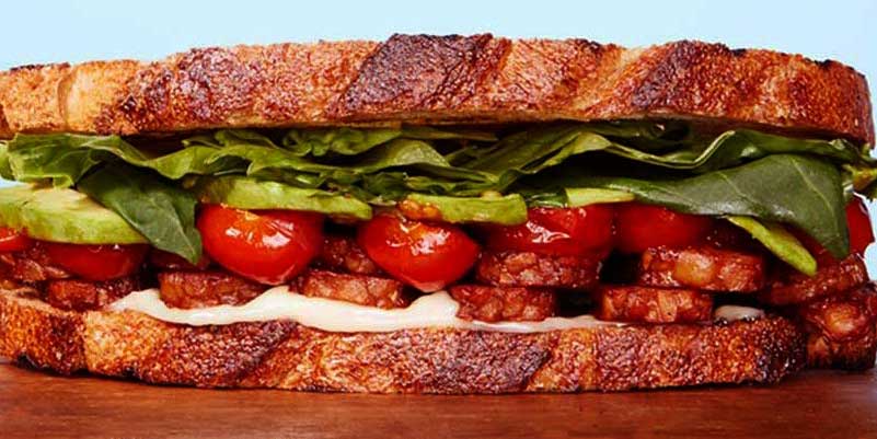 bocadillo con ingredientes como lechuga, tomate, tempeh y salsa