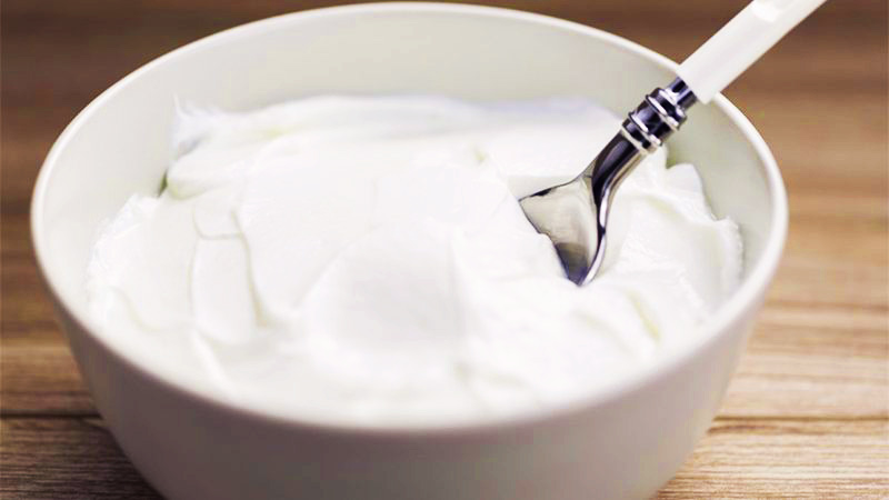 yogur en un bol blanco, con una cuchara y sobre una mesa de madera