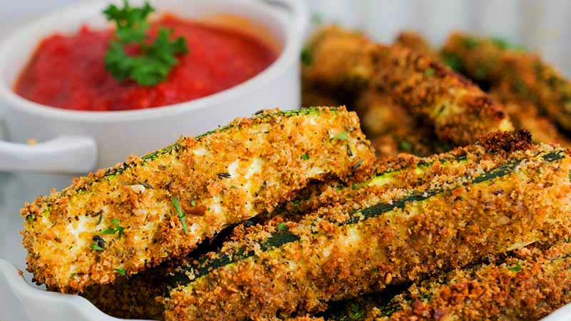 palitos de calabacín rebozados con un bol con tomate al fondo