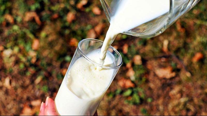 una mano sosteniendo un vaso y una jarra vertiendo la leche en el vaso