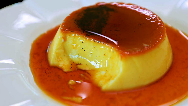 flan pequeño con caramelo y con un trozo cortado sobre un plato blanco