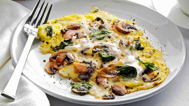 revuelto de huevo con setas y verduras en un plato blanco con un tenedor al lado