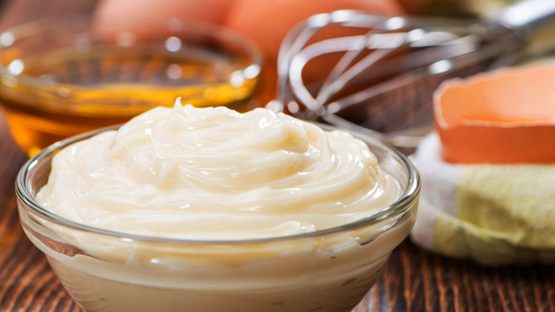 mayonesa en un bol de cristal con un bol de aceite al fondo, difuminado, huevos y varillas