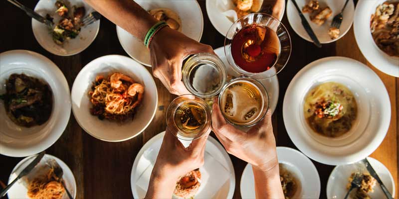 Mesa vista desde arriba con muchos platos con comida y cuatro personas chocando sus copas