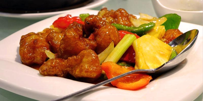 un plato blanco con trozos de cerdo con salsa y verduras
