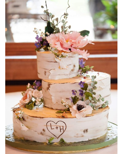 Tarta de tres pisos simulando un tronco de un árbol con las iniciales de los novios grabadas