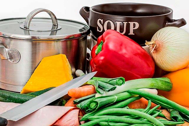 mesa de cocina con olla, verduras y cuchillo preparados para cocinar